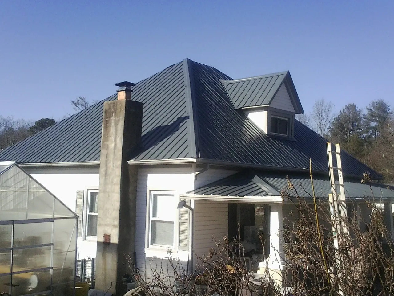 Dark blue standing seam metal roof on a white farmhouse with dormer — Slate & Tile Roof Repair by Roofing Brothers in Wysox