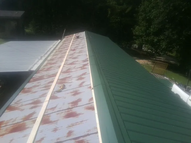 Old rusted panels beside newly installed green metal roofing — Wind Damage Roof Repair by Roofing Brothers in Wysox