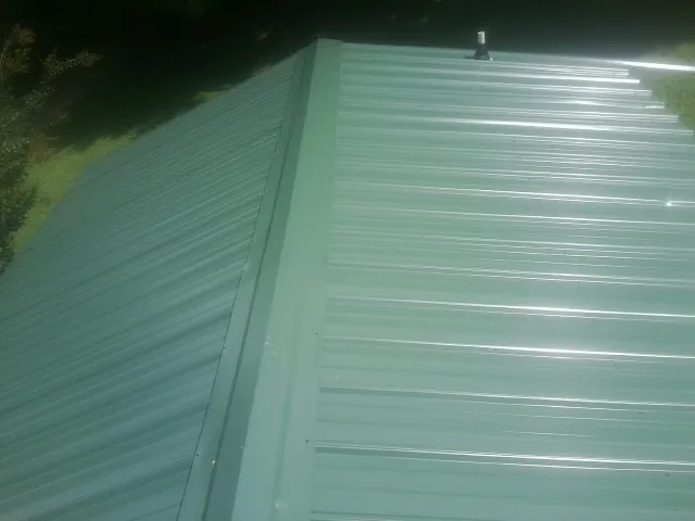 New green metal panels meeting at the ridge of a roof — Flat Roof Repair work by our crew in Wysox