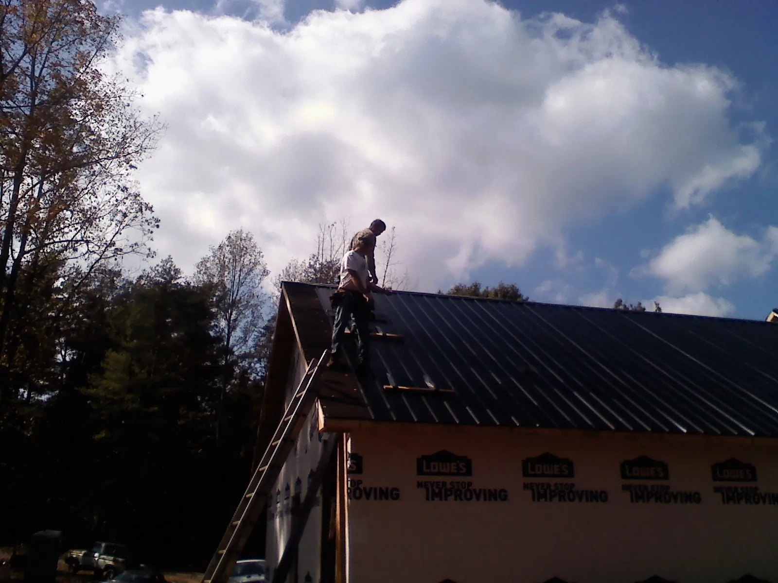 Roofer fastening dark metal panels high against a cloudy sky, from a Roof Inspection job in Wysox