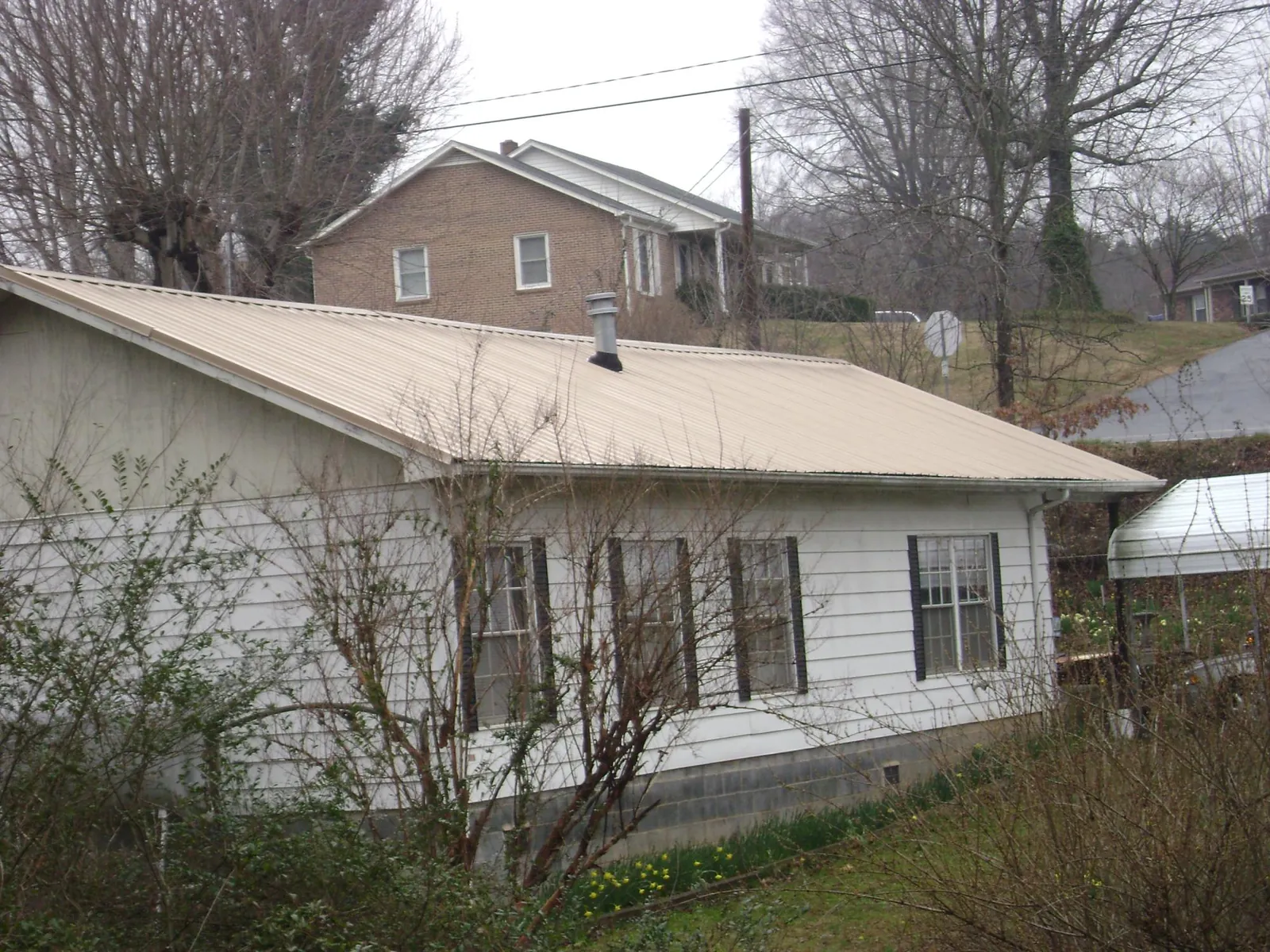 Tan metal roof on a white sided house set into a hillside — Commercial Roofing by Roofing Brothers in Wysox
